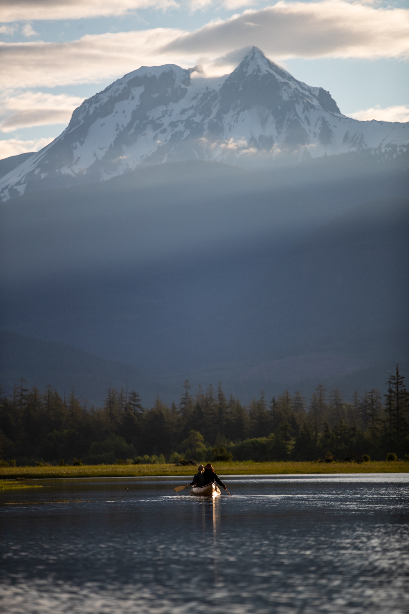 A canoeist on a calm lake below a snow-capped mountain on a moody day