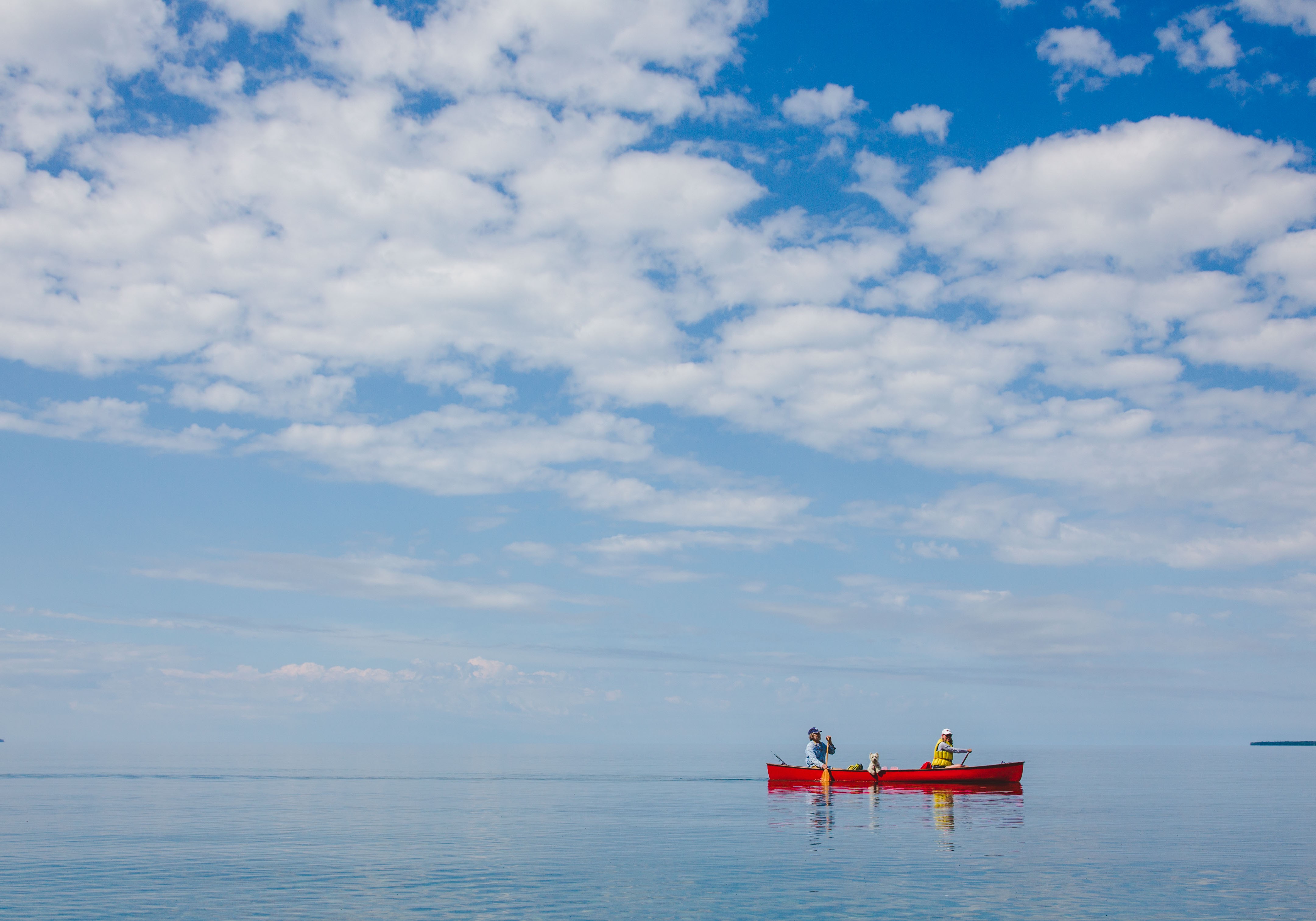 A red canoe on calm water under a big blue sky