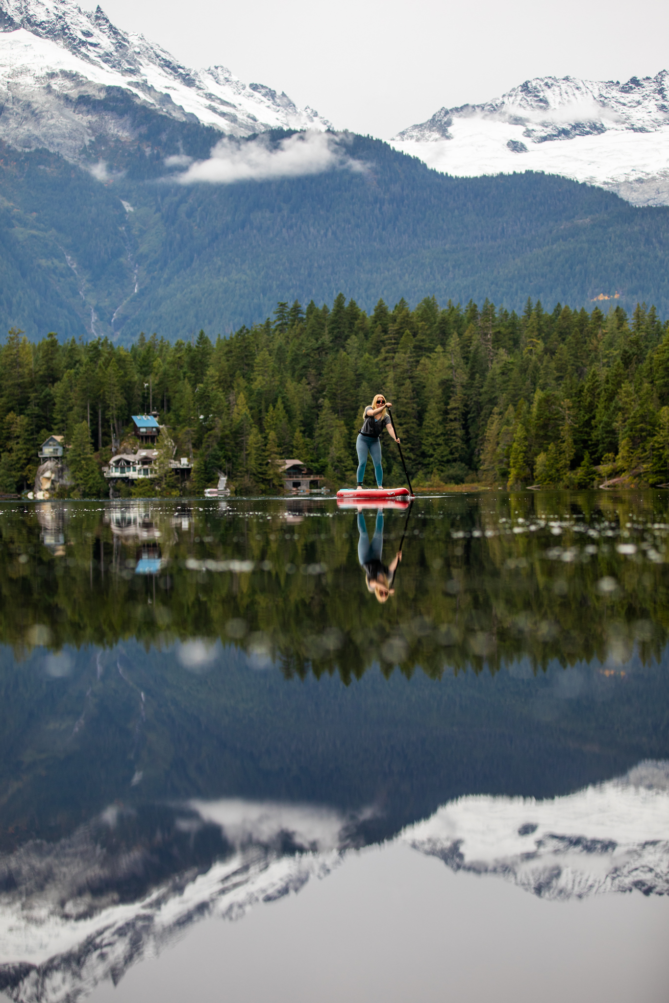 Paddleboarder on a mirror-calm lake with mountains reflected